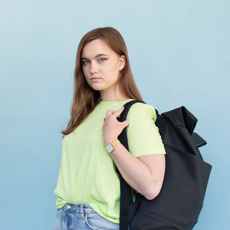 Student voor een blauwe muur met haar tas over haar schouder