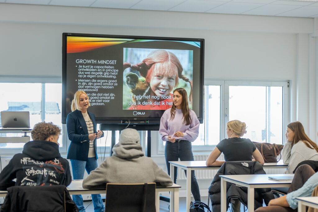 Studenten presenteren voor een grote groep.