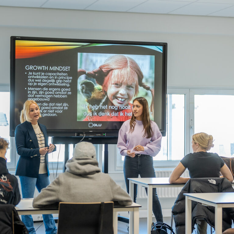 Studenten presenteren voor een grote groep.