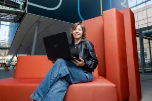 Student AV-specialist is in het atrium op de rode bank bezig met het bewerken van een video