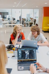 Studenten werken samen aan de opdracht op de gang van het Grafisch Lyceum Utrecht.